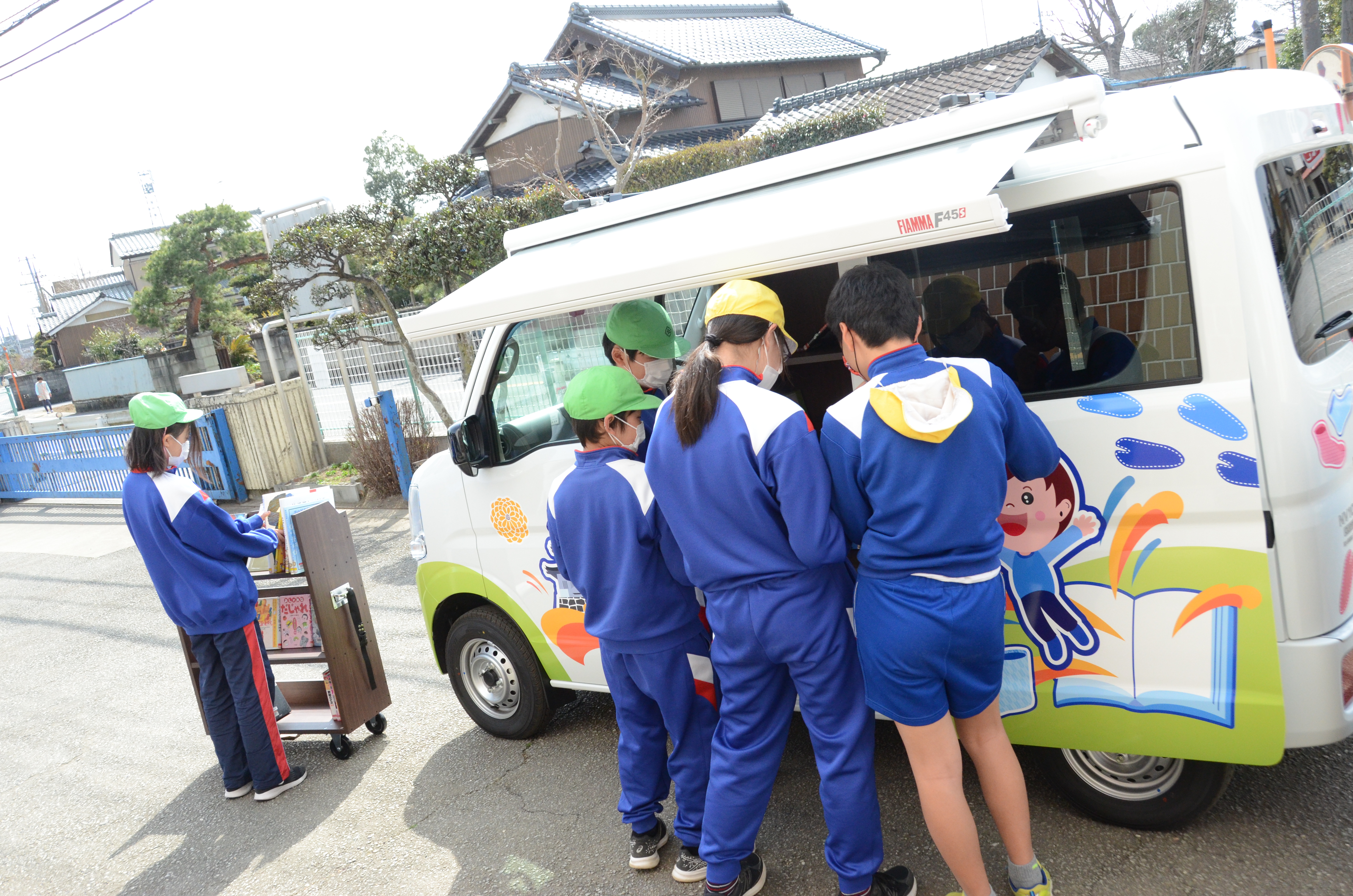 たびりん号に並んで本を読む小学生の子どもたち